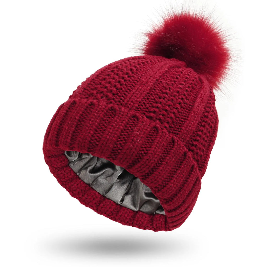 Woman wearing a light grey wool beanie with a faux fur pom pom and satin lining.