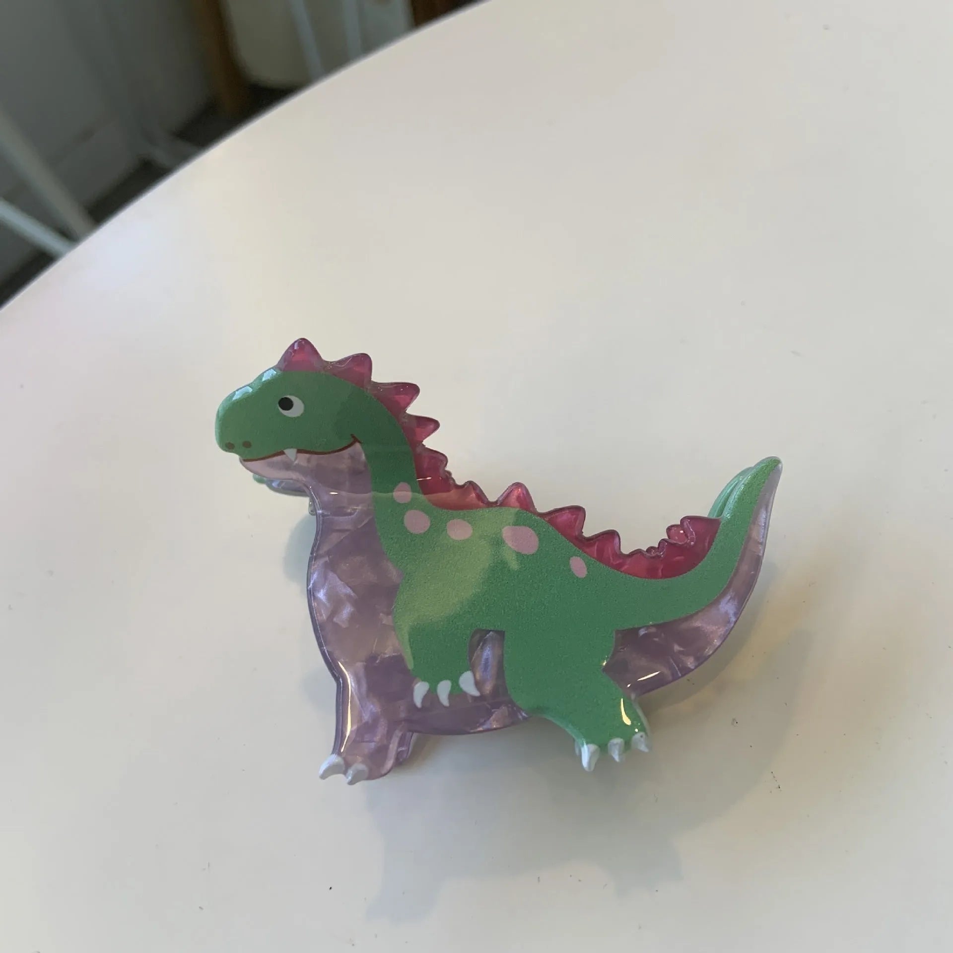 A colourful acrylic jaw clip hair grip featuring a detailed little dinosaur design.