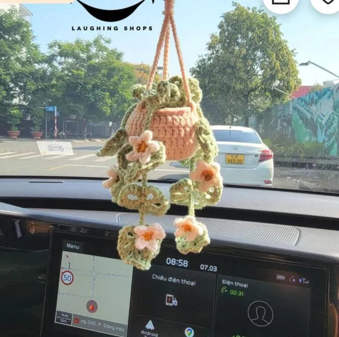 Green and white knitted wool car plant decoration with hanging rope on car dashboard