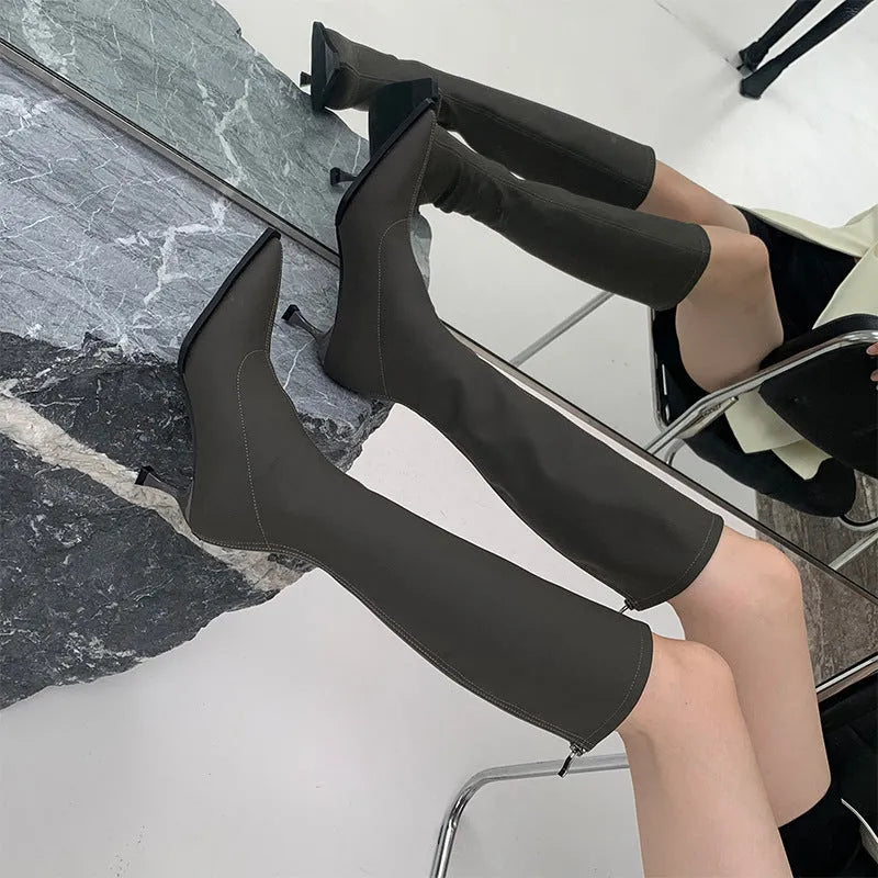 Black pointed toe below knee stiletto heel boots with a back zipper on a woman's leg.