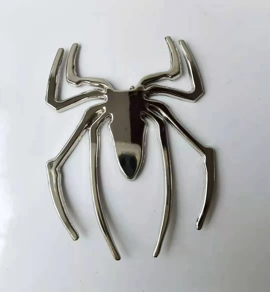 Three-dimensional metal spider-shaped bumper sticker in silver finish on a white background.