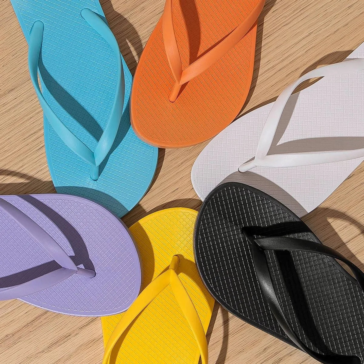 Orange foldable beach slippers with a hollow-out plastic upper and non-slip PVC sole on a sandy background.