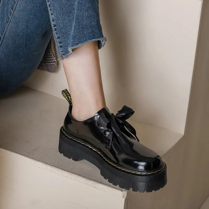 Women's black thick soled lace-up shoes with ribbon detail on a white background