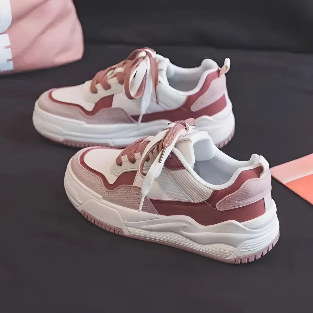 Pink and beige low top women's sneakers with a rubber sole on a neutral background.