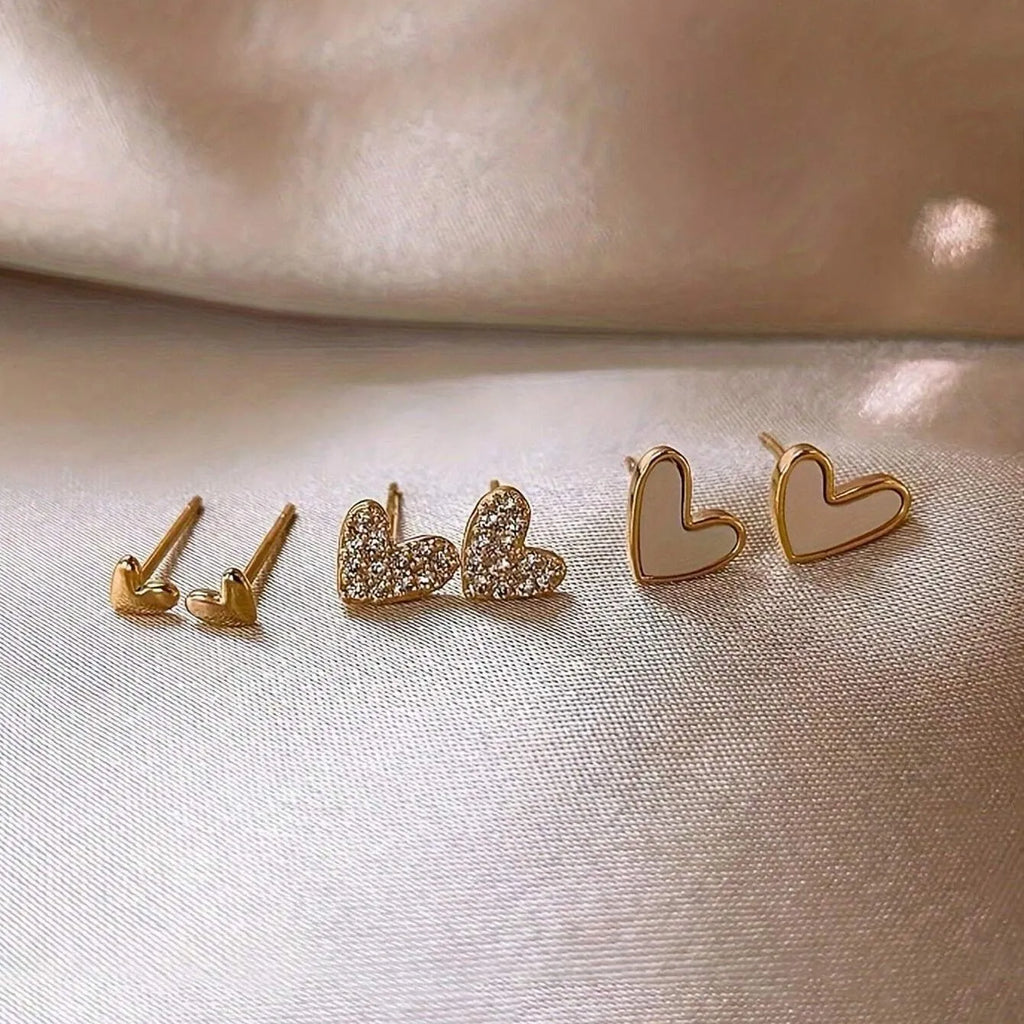 Set of three pairs of women's heart-shaped stud earrings in gold, black, white, and pink.