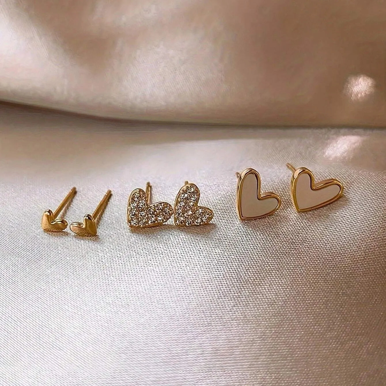 Set of three pairs of women's heart-shaped stud earrings in gold, black, white, and pink.