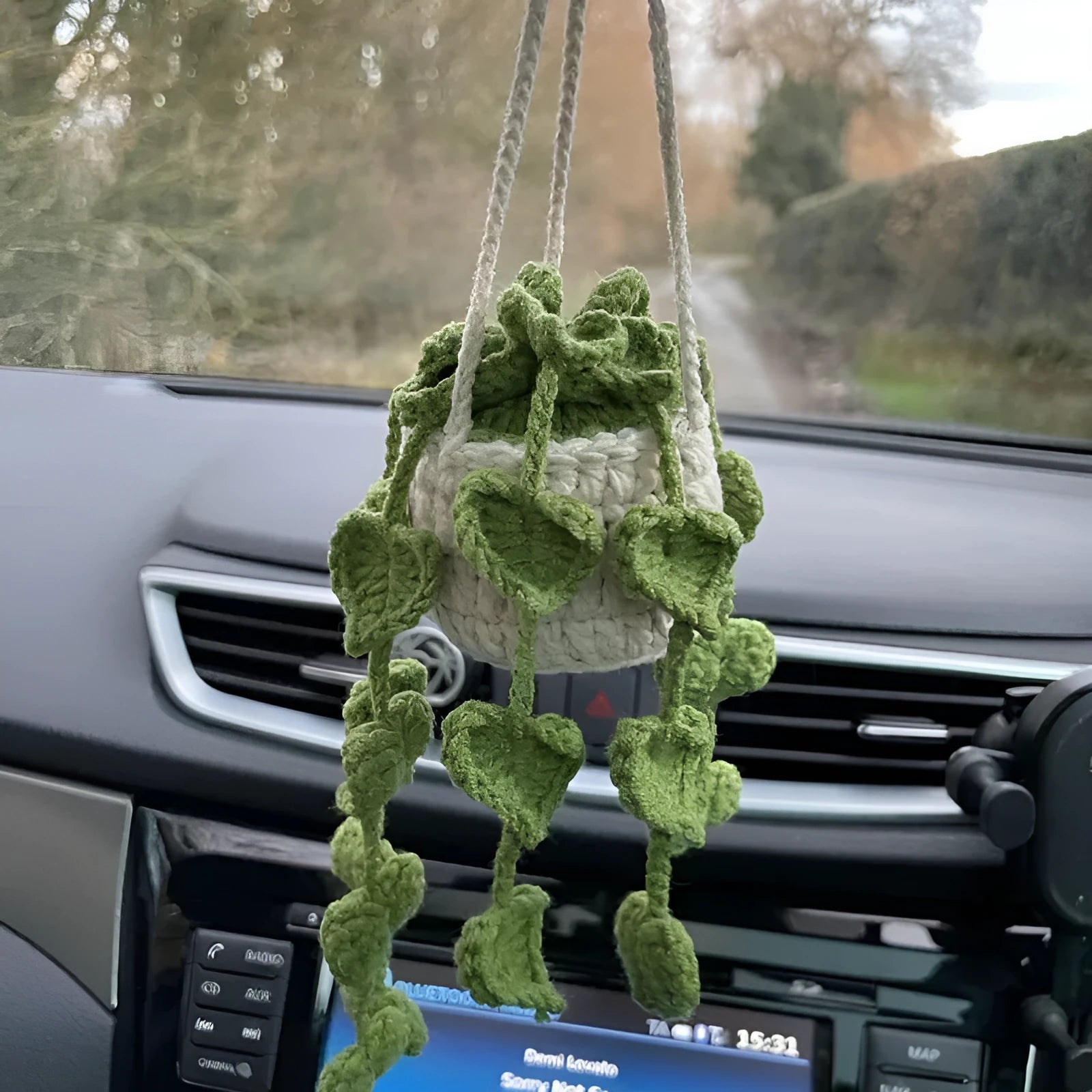 Green and white knitted wool car plant decoration with hanging rope on car dashboard