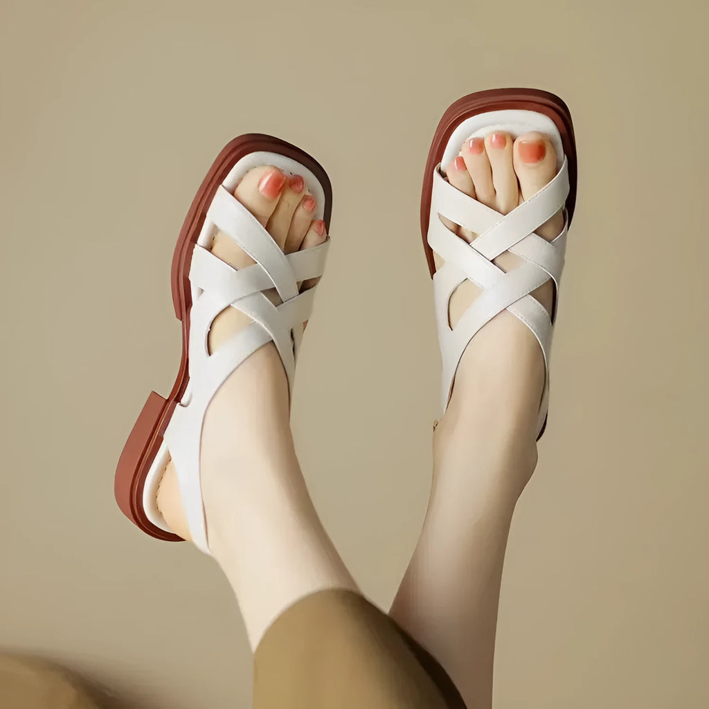 Women's glossy patent leather square-toe sandals with cross-strap fastening on a neutral background