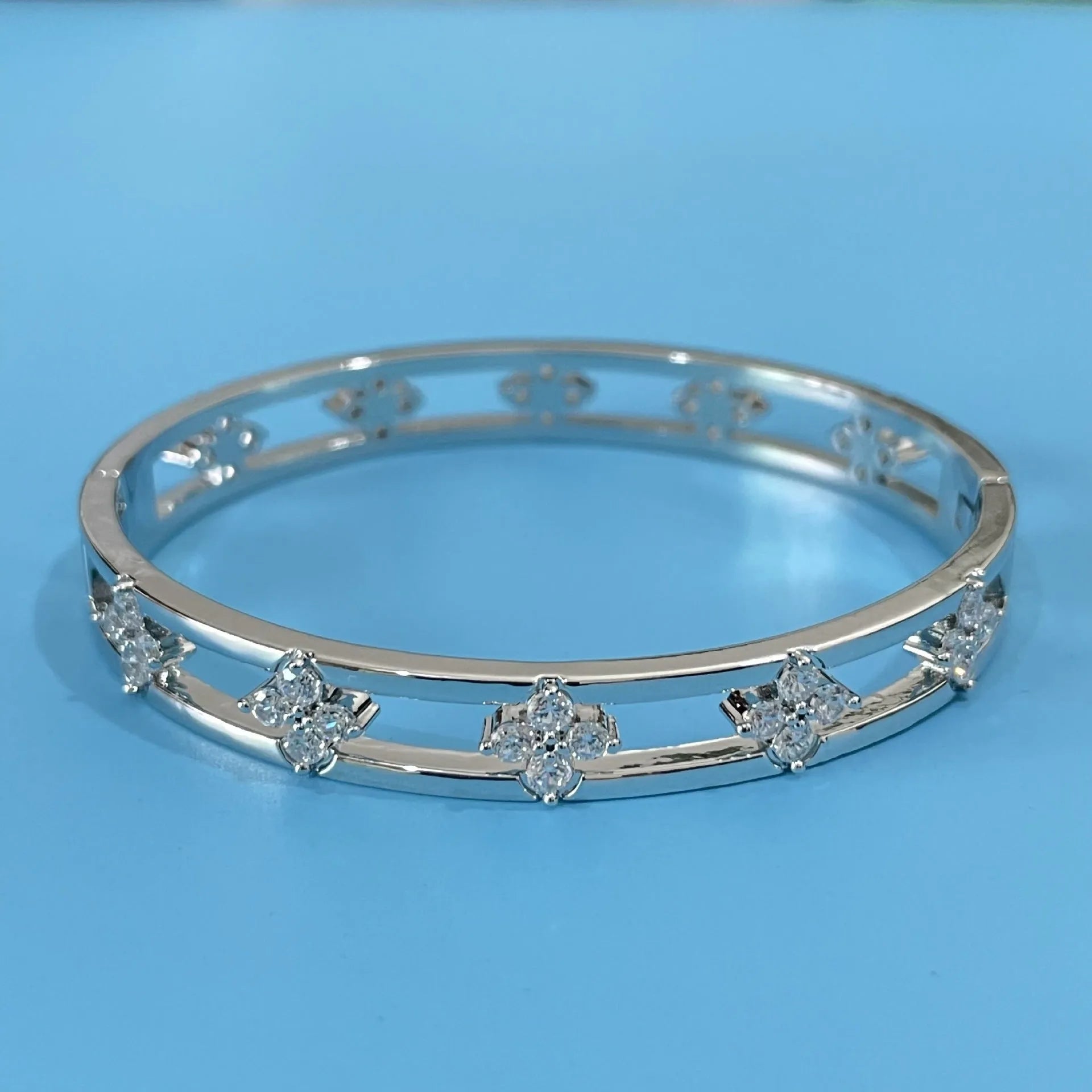 Gold or silver adjustable hollow bracelet with a four-leaf clover charm inlaid with a zircon stone.