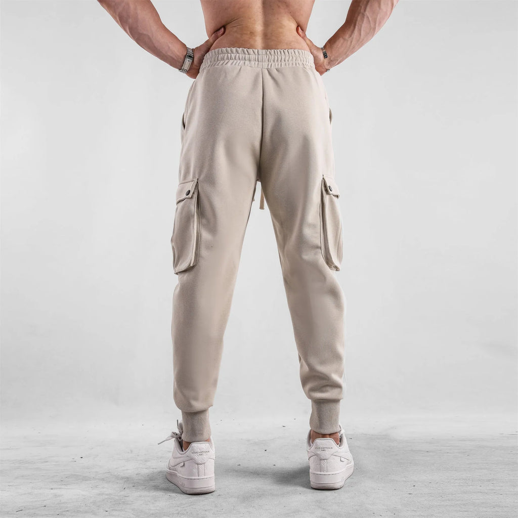 Man wearing loose light grey cotton trousers with ankle tie and multiple pockets, style of American sports leisure wear.