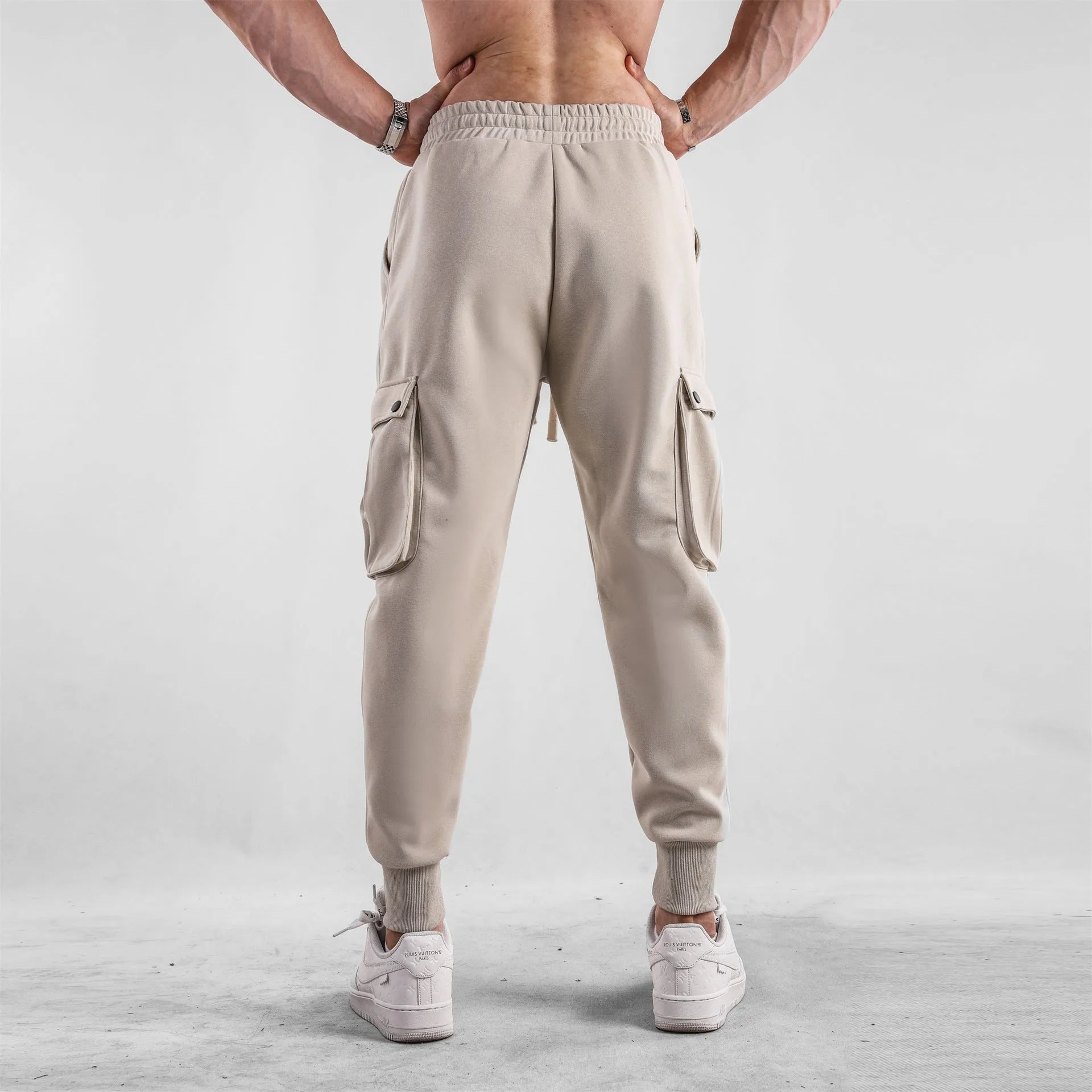 Man wearing loose light grey cotton trousers with ankle tie and multiple pockets, style of American sports leisure wear.