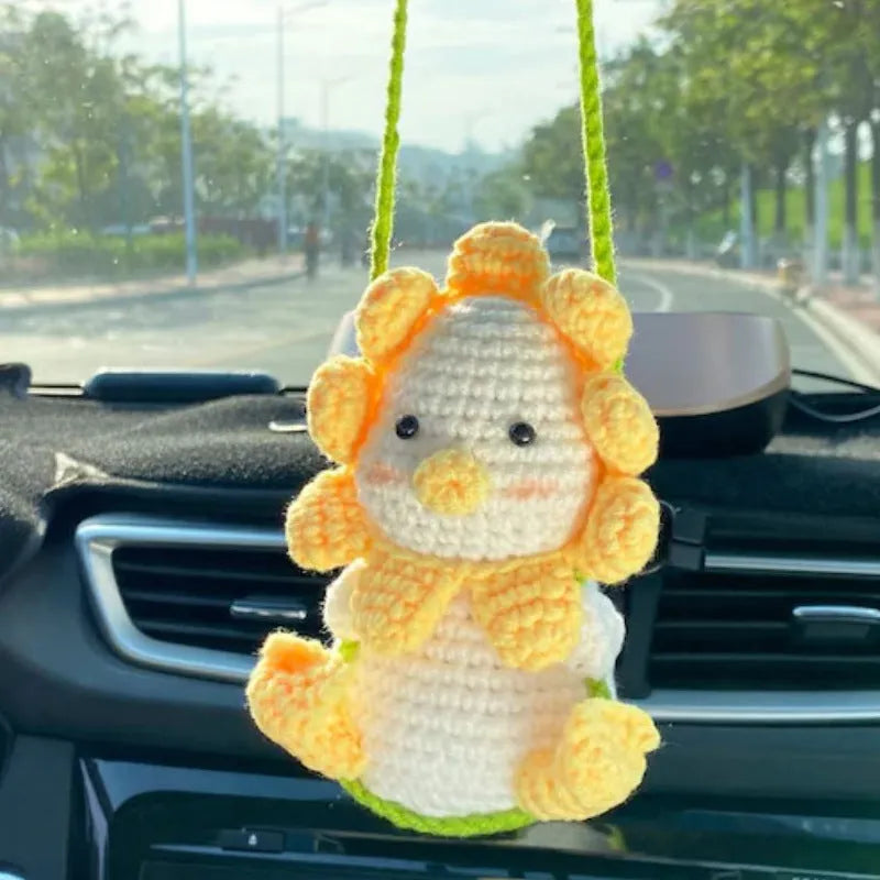 Green and white knitted wool car plant decoration with hanging rope on car dashboard