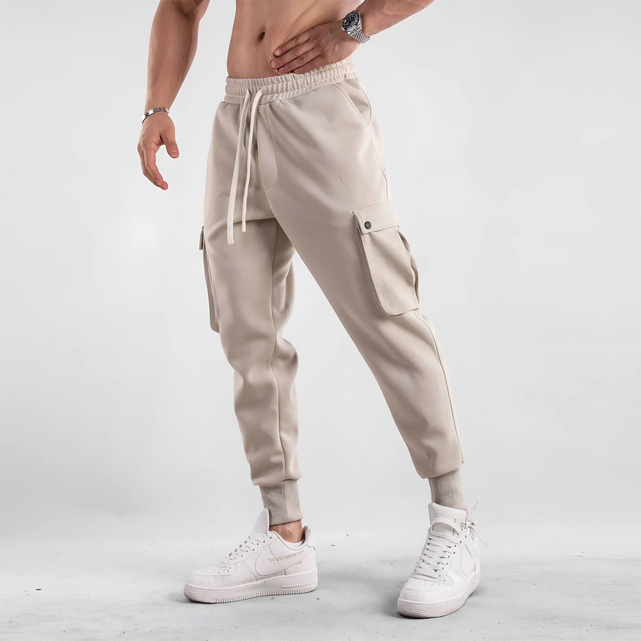 Man wearing loose light grey cotton trousers with ankle tie and multiple pockets, style of American sports leisure wear.