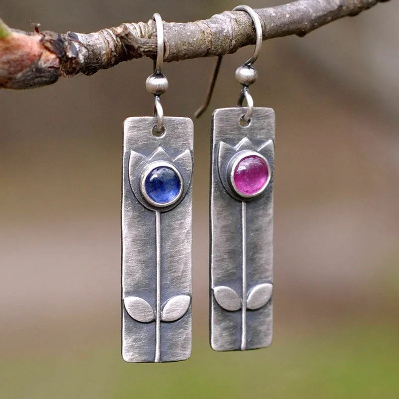 A pair of antique finish red sapphire earrings with a geometric shape and oval details on a white background.