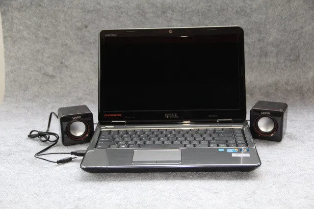 Black square USB computer speaker on desktop next to monitor