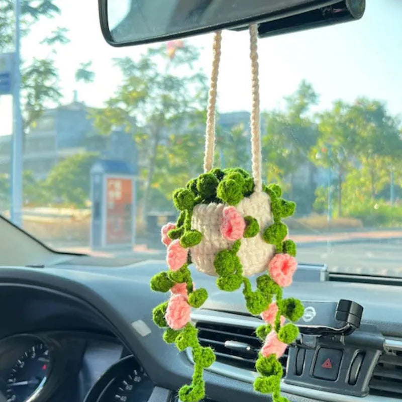 Green and white knitted wool car plant decoration with hanging rope on car dashboard