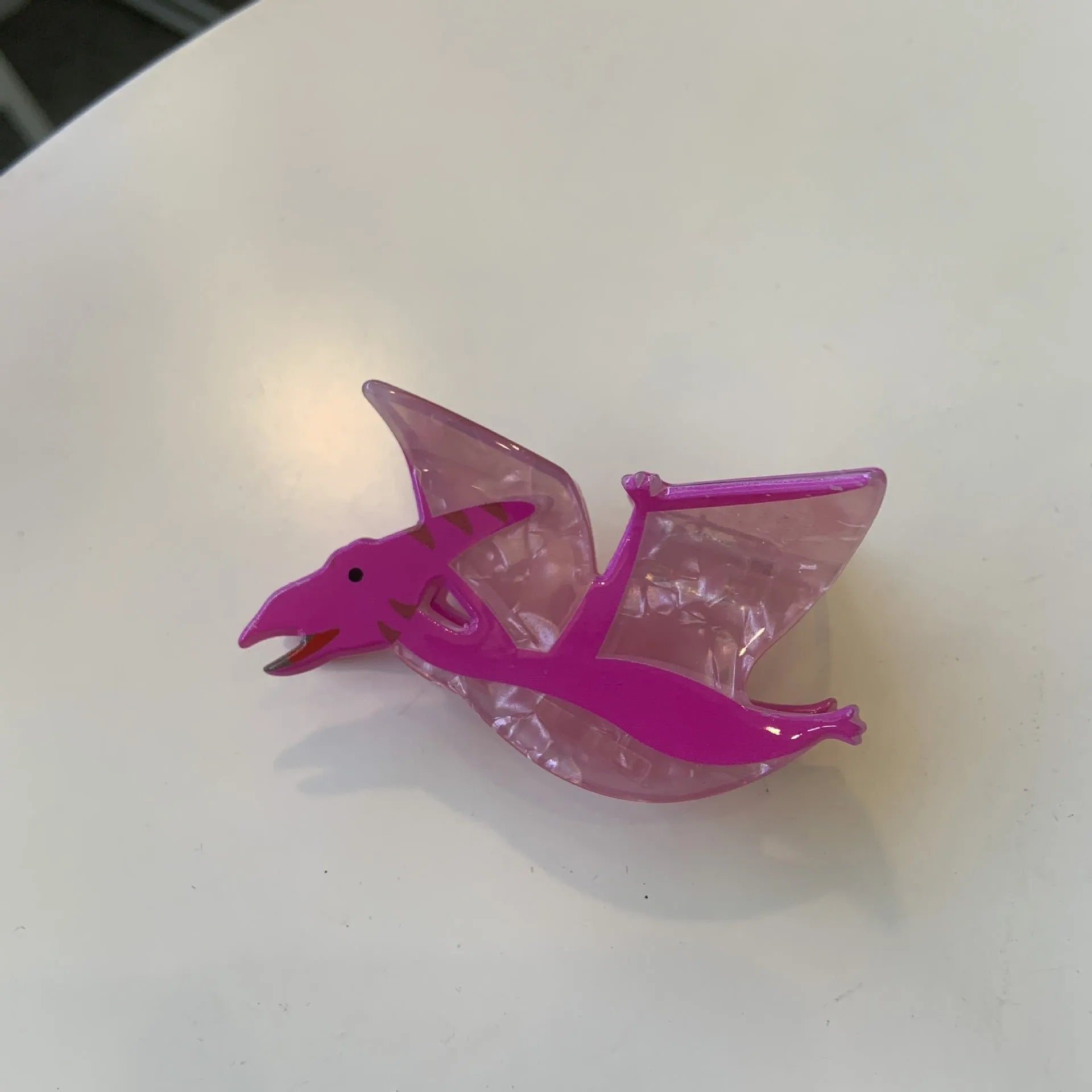 A colourful acrylic jaw clip hair grip featuring a detailed little dinosaur design.