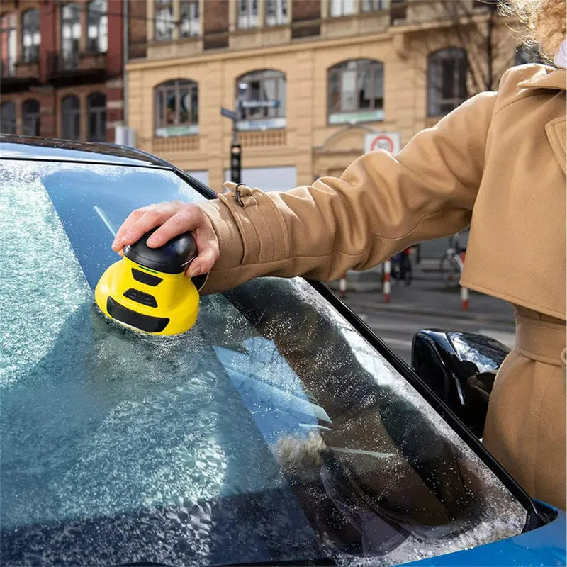Yellow cordless electric ice scraper with USB charging cable on a car windscreen.