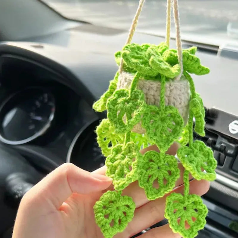Green and white knitted wool car plant decoration with hanging rope on car dashboard