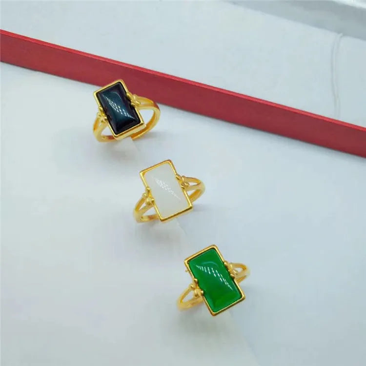 Adjustable brass gold-plated ring with a central green artificial gemstone on a finger.