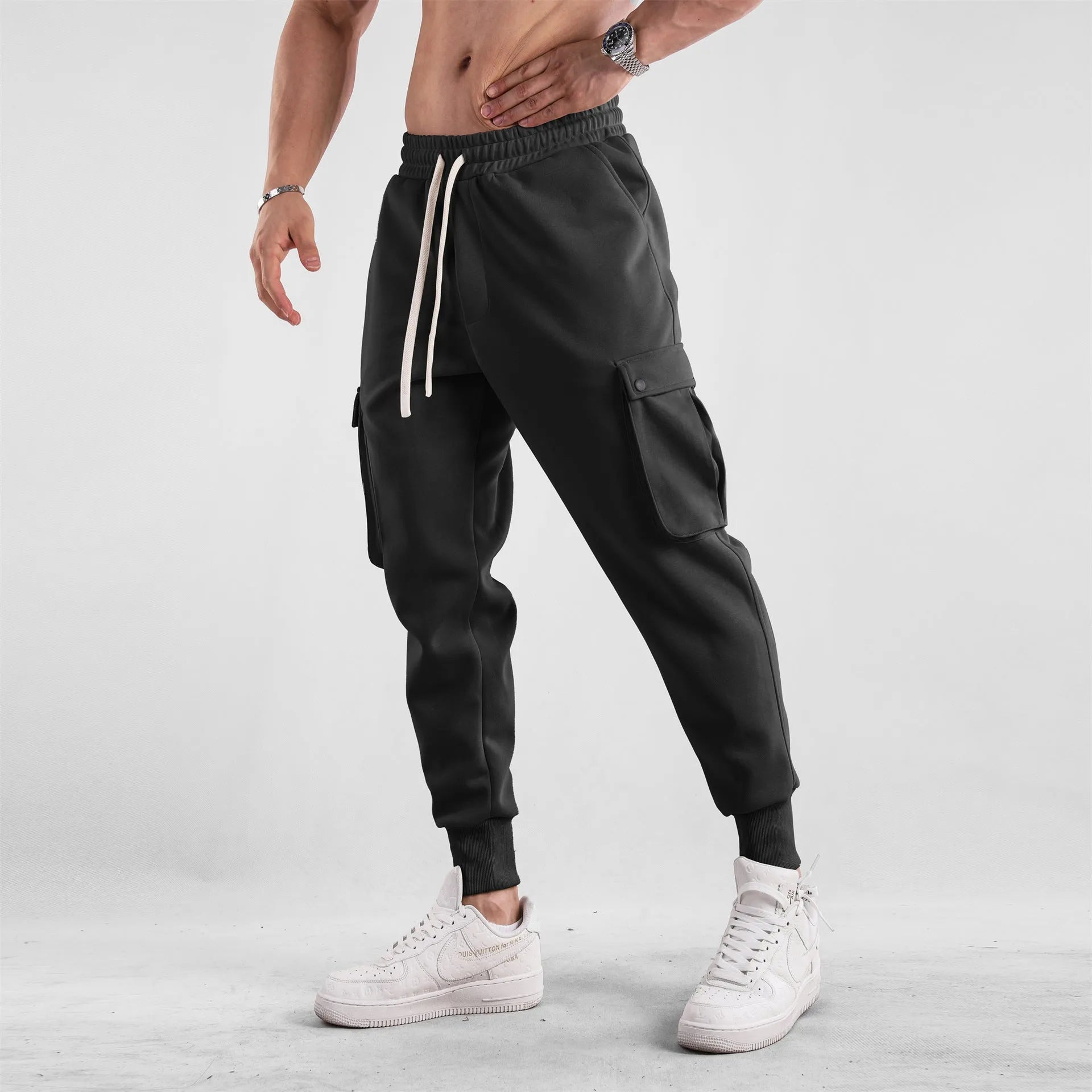 Man wearing loose light grey cotton trousers with ankle tie and multiple pockets, style of American sports leisure wear.