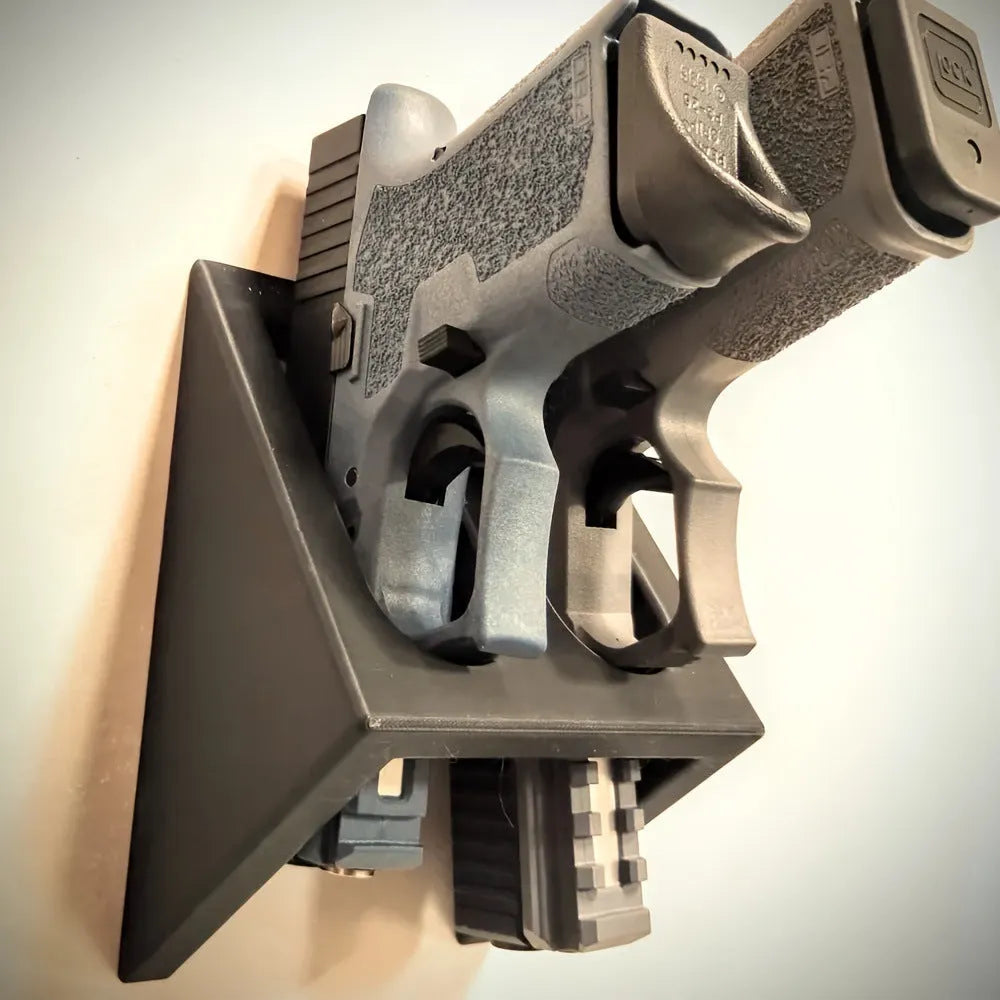 Black punk-style plastic pistol display stand on a surface, showing its compact size and cradle design.