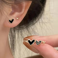 Set of three pairs of women's heart-shaped stud earrings in gold, black, white, and pink.