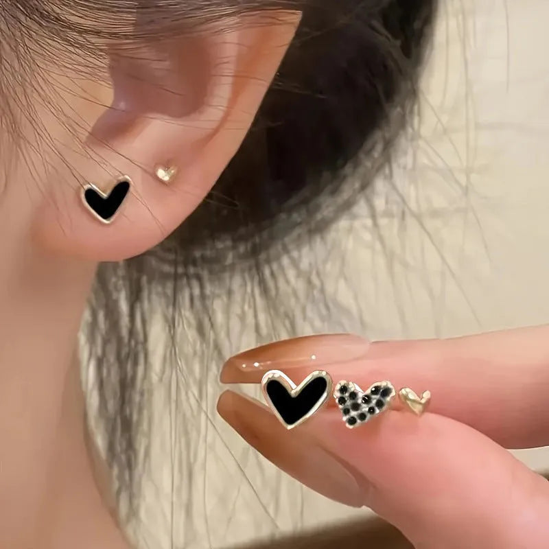 Set of three pairs of women's heart-shaped stud earrings in gold, black, white, and pink.