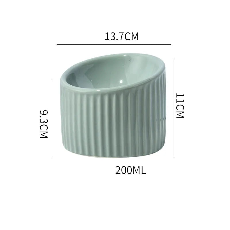 Dark green elevated ceramic cat bowl on a wooden floor, showing its raised height and round, whisker-friendly shape.