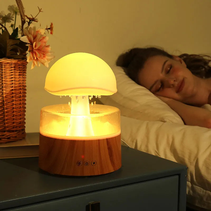 White cloud-shaped humidifier diffuser with LED rain effect and remote control on a wooden table.