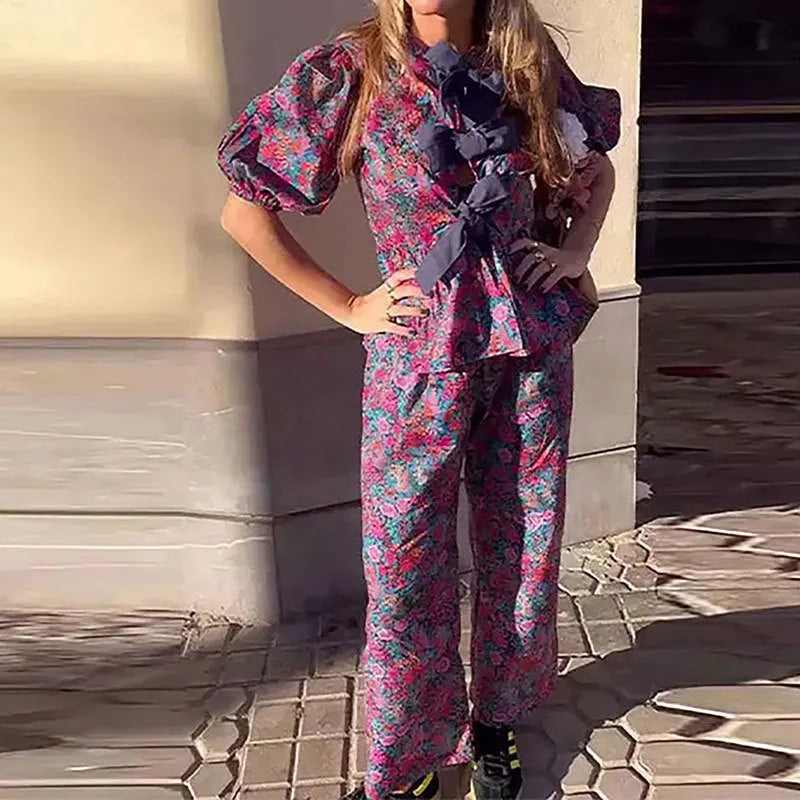 Floral print two-piece leisure suit with tie-neck blouse, puff sleeves, and long trousers.