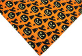Black and orange reversible Halloween dog bandana with pumpkin and spider web patterns lying flat.