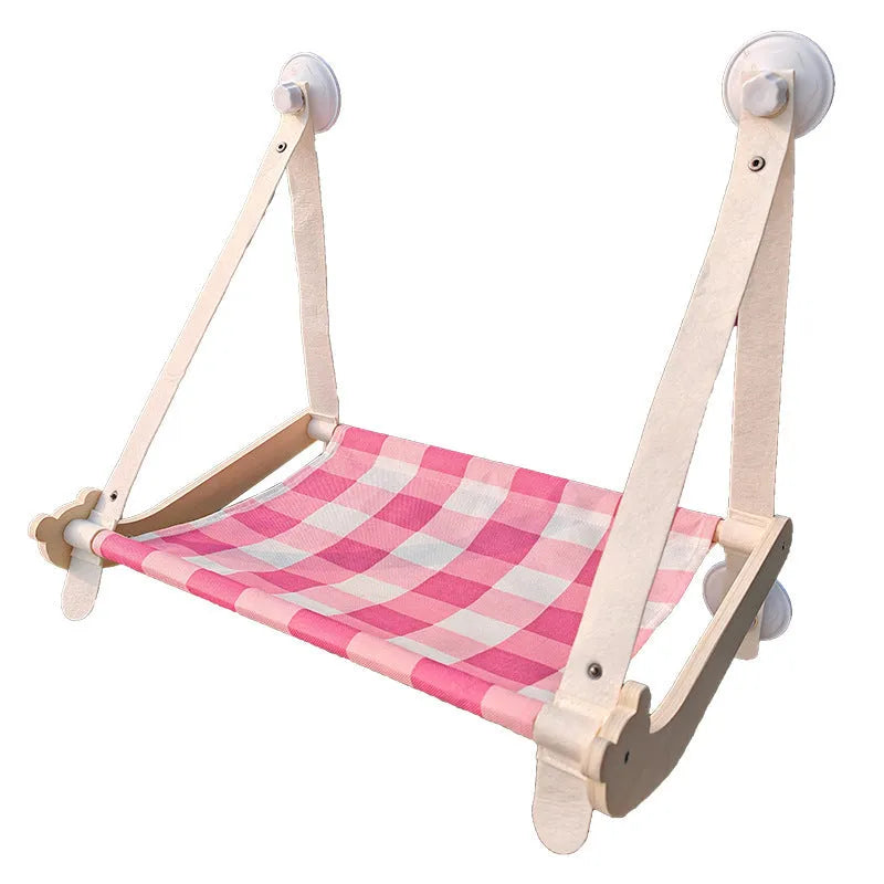 Pink wooden cat hammock with suction cups attached to a window, showing a cat resting on the linen fabric.