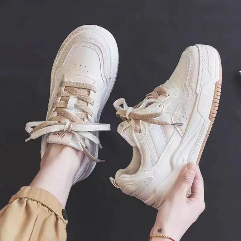 Pink and beige low top women's sneakers with a rubber sole on a neutral background.