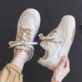 Pink and beige low top women's sneakers with a rubber sole on a neutral background.