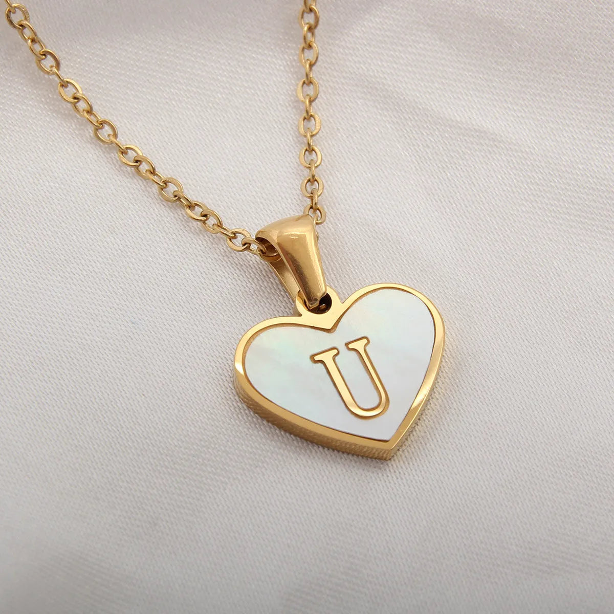 Gold-plated heart necklace with white shell pendant personalised with a letter, on an adjustable chain.