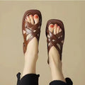 Women's glossy patent leather square-toe sandals with cross-strap fastening on a neutral background