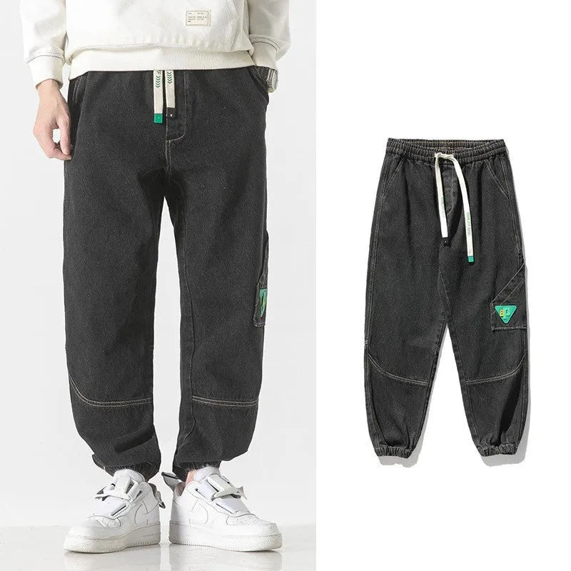 Men's loose fit tapered cotton trousers in black, shown on a model, featuring a mid-waist and tapered leg design.