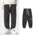 Men's loose fit tapered cotton trousers in black, shown on a model, featuring a mid-waist and tapered leg design.