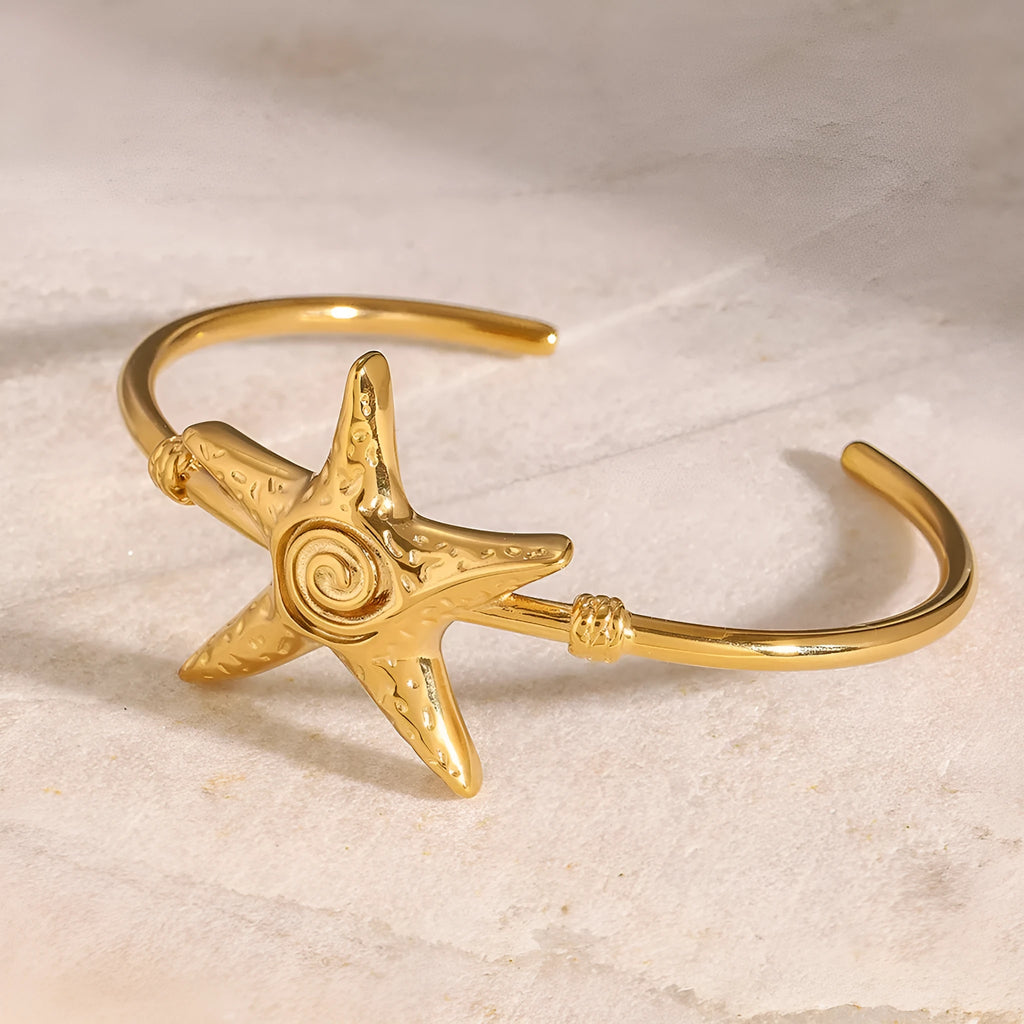 Stainless steel open-ended bracelet with starfish charm on a flat surface