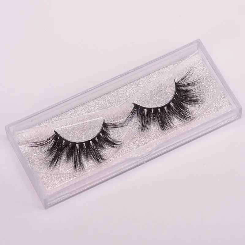 A pair of 5D style false eyelashes made from mink hair, shown with a double-headed brush and a black hair cap.