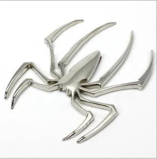Three-dimensional metal spider-shaped bumper sticker in silver finish on a white background.