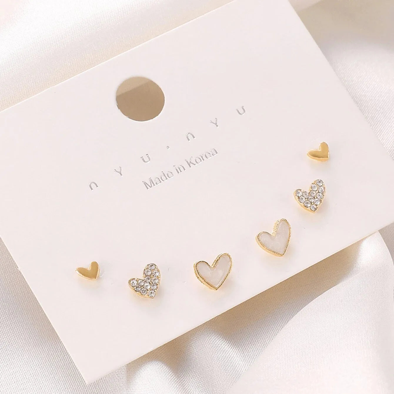 Set of three pairs of women's heart-shaped stud earrings in gold, black, white, and pink.