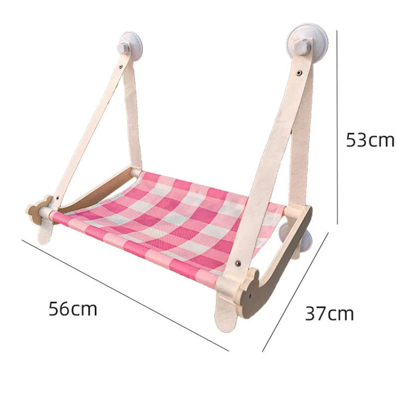 Pink wooden cat hammock with suction cups attached to a window, showing a cat resting on the linen fabric.
