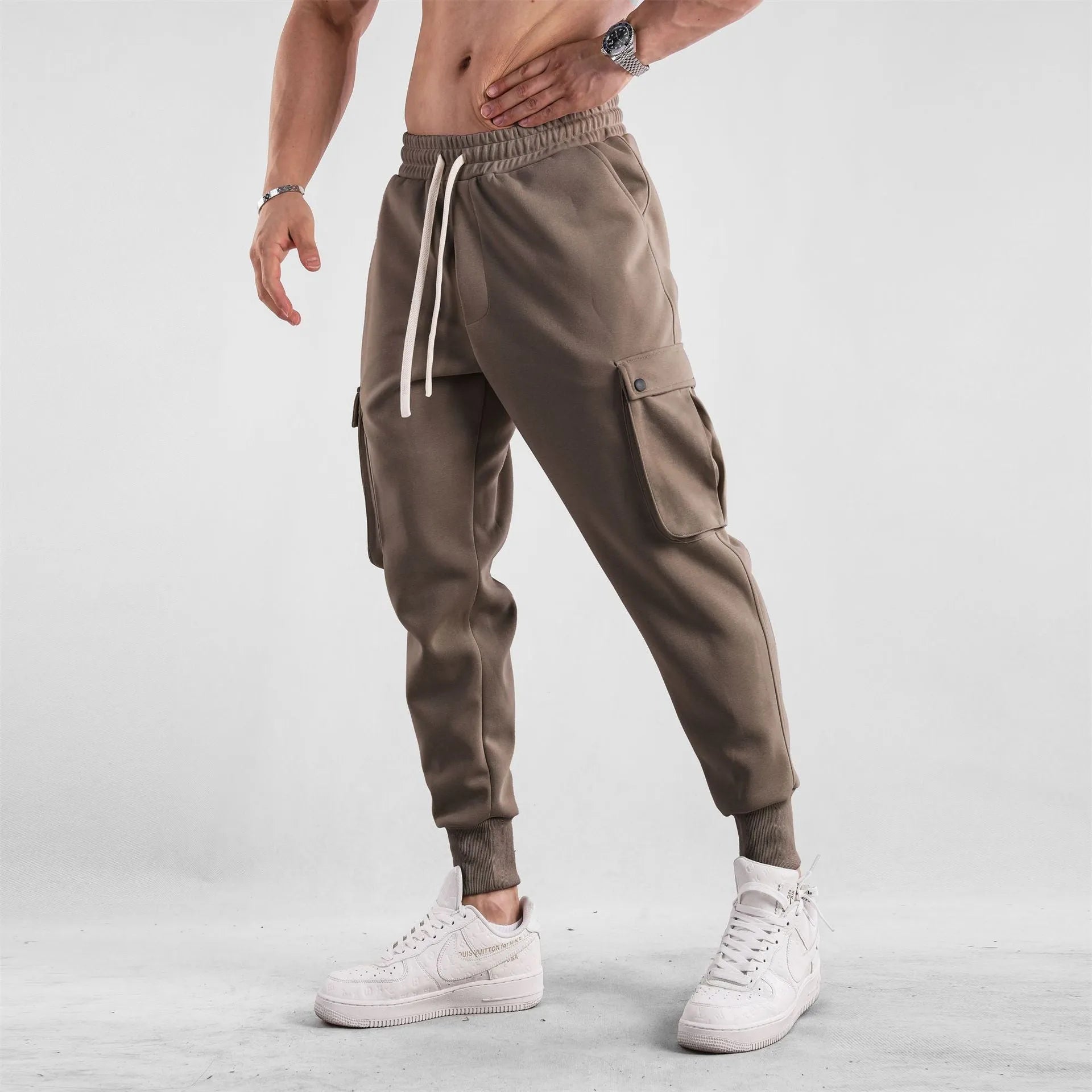 Man wearing loose light grey cotton trousers with ankle tie and multiple pockets, style of American sports leisure wear.