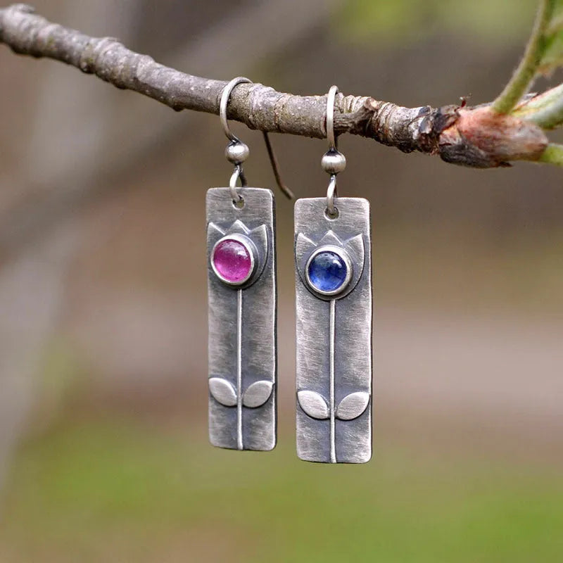 A pair of antique finish red sapphire earrings with a geometric shape and oval details on a white background.