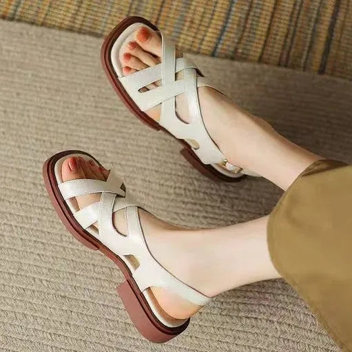 Women's glossy patent leather square-toe sandals with cross-strap fastening on a neutral background