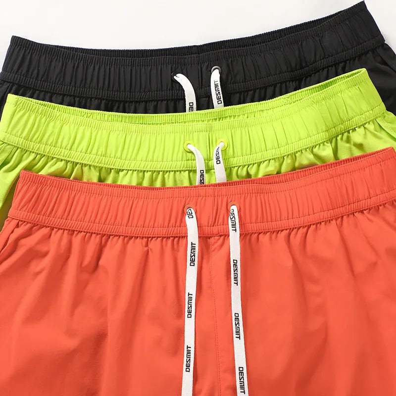 Man wearing loose orange red polyester shorts on a beach, demonstrating the micro-elastic fit.