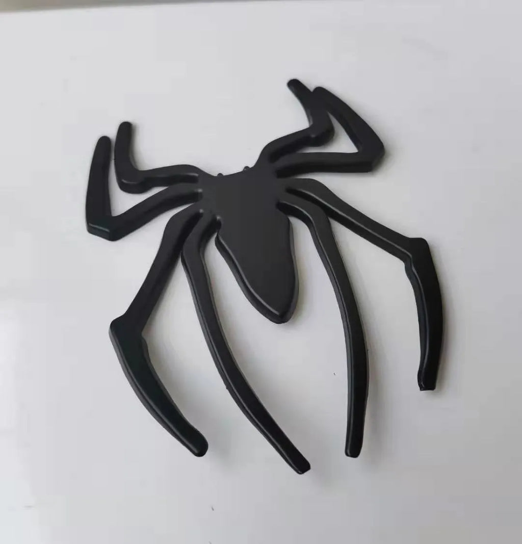 Three-dimensional metal spider-shaped bumper sticker in silver finish on a white background.