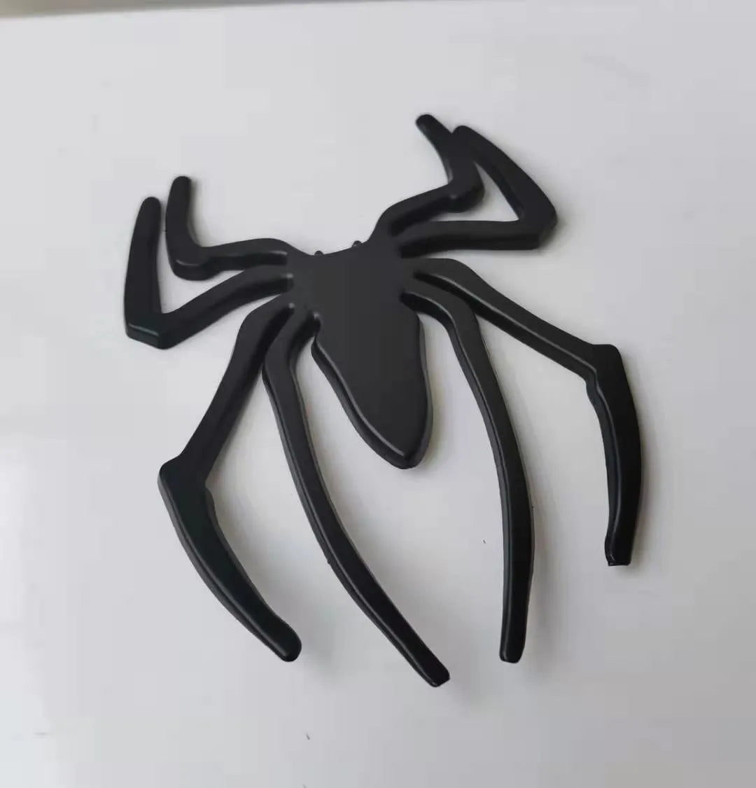 Three-dimensional metal spider-shaped bumper sticker in silver finish on a white background.